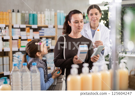 Middle-aged woman with daughter choosing cream in drugstore Middle-aged woman with daughter choosing cream in drugstore 125604247