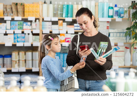 Woman scans a set of toothbrushes at a pharmacy next to her child 125604272