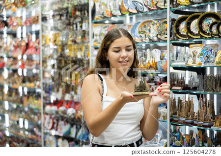 Female buyer holds in hands tests metal figurine Sagrada familia in memorable gifts shop 125604278