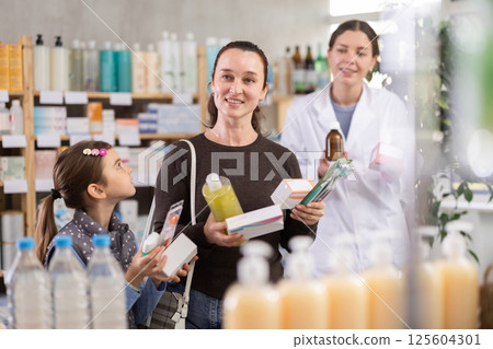 Middle-aged woman with daughter choosing pills in drugstore 125604301