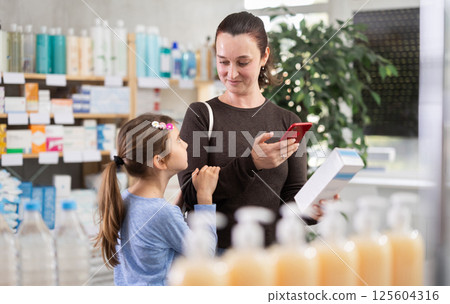 Woman with daughter in pharmacy scans QR code on cream Woman with daughter in pharmacy scans QR code on cream 125604316