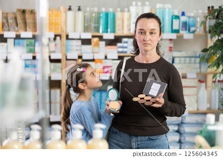 woman and daughter choose cosmetics in a pharmacy near the shelves woman and daughter choose cosmetics in a pharmacy near the shelves 125604345