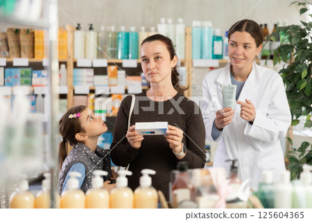 Mother choosing healing ointment for daughter at pharmacy 125604365
