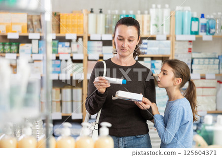 woman and her daughter choose an ointment at a pharmacy near the counter woman and her daughter choose an ointment at a pharmacy near the counter 125604371