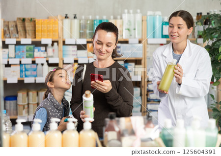 Middle-aged woman with daughter scanning barcode on shampoo in drugstore Middle-aged woman with daughter scanning barcode on shampoo in drugstore 125604391
