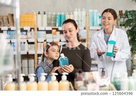 Middle-aged woman with daughter choosing mouthwash liquid in drugstore 125604396