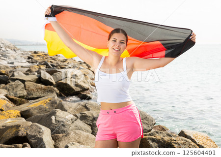 Happy woman on sea beach with Germany flag on sunny day Happy woman on sea beach with Germany flag on sunny day 125604401