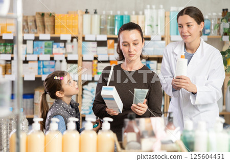 Middle-aged woman with daughter choosing cream in drugstore 125604451