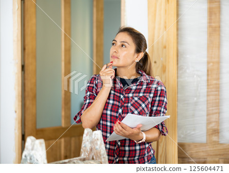 Woman inspecting rooms in building site, checking documents Woman inspecting rooms in building site, checking documents 125604471
