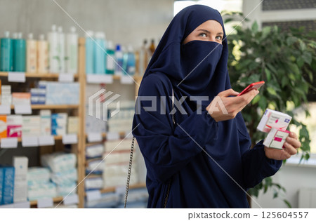 Young Muslim woman customer scanning QR-code on paracetamol box 125604557