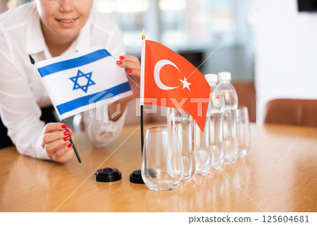 Female employee of the delegation sets flags of countries of Turkey and Israel on the table before start of negotiations 125604681