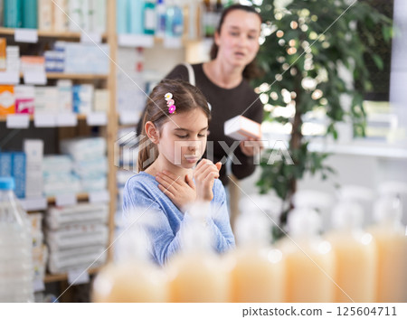 child stands and coughs in the pharmacy, and the mother chooses medications child stands and coughs in the pharmacy, and the mother chooses medications 125604711