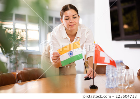 Young female assistant putting up swiss and indian flags on table for international negotiations 125604718