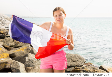 Young happy woman holding flag of French with a happy face and smiling on seashore on sunny day 125604723