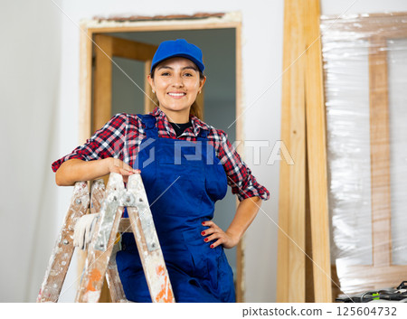 Young woman builder posing next to a stepladder in room being renovated 125604732