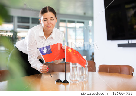 Young woman putting flags of Taiwan and China on table in office Young woman putting flags of Taiwan and China on table in office 125604735