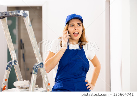 Smiling young workwoman talking on phone at construction site indoors Smiling young workwoman talking on phone at construction site indoors 125604741