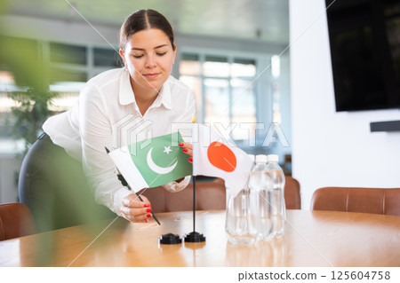 Positive young woman putting little flag of Pakistan on table next to the flag of Japan 125604758