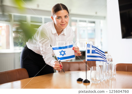 Young woman putting flags of Israel and Greece on table in office 125604760