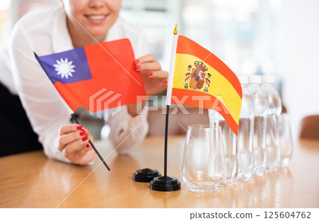Unrecognizable girl sets midget flags of Spain and Taiwan before international negotiations 125604762