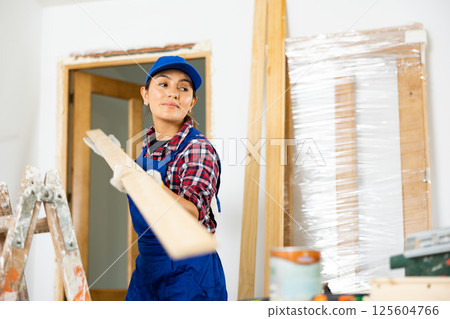 Cheerful female repairer carrying bunch of wooden planks Cheerful female repairer carrying bunch of wooden planks 125604766
