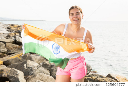 Pretty young girl holding the India flag in her hands on the beach on sunny day Pretty young girl holding the India flag in her hands on the beach on sunny day 125604777