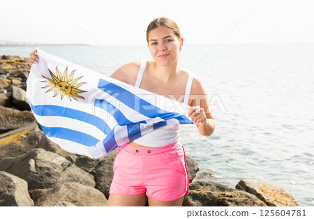 Young woman on coast posing with flag of Uruguay 125604781