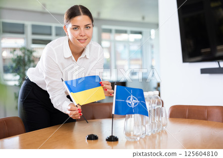 Young woman puts flags of Ukraine and NATO on table in office 125604810
