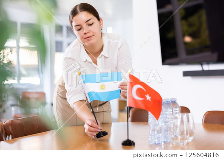 Positive young woman putting flag of Argentina on the table with flag of Turkey in conference room 125604816