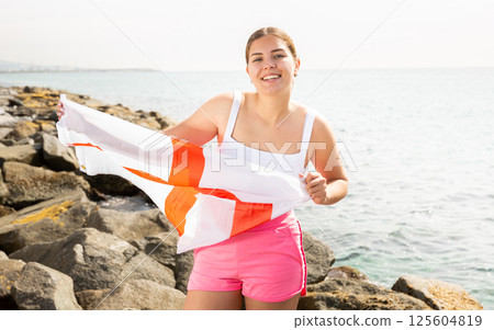 Portrait of positive girl with the flag of England on the seashore on sunny day Portrait of positive girl with the flag of England on the seashore on sunny day 125604819