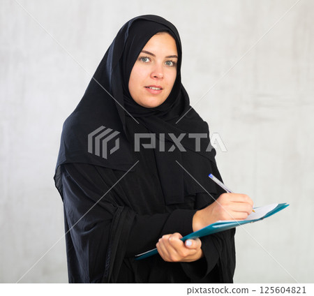 imperturbable girl in hijab holds several notebooks and writes important note in her diary imperturbable girl in hijab holds several notebooks and writes important note in her diary 125604821