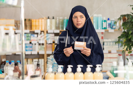 Young woman in khimar examining medicine box at pharmacy Young woman in khimar examining medicine box at pharmacy 125604835