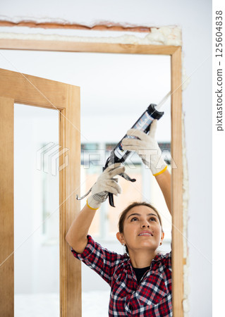 Woman herself fills the gaps with mounting foam - installation of new doors in room Woman herself fills the gaps with mounting foam - installation of new doors in room 125604838