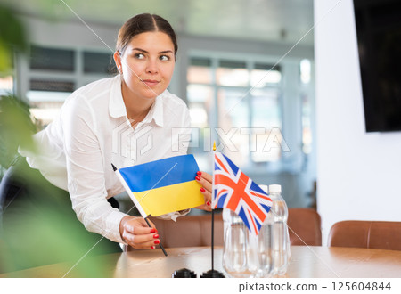 Positive young woman putting little flag of Ukraine on table next to the flag of Great Britain Positive young woman putting little flag of Ukraine on table next to the flag of Great Britain 125604844