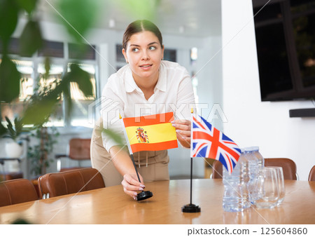 Young woman puts flags of Spain and Great Britain on table 125604860