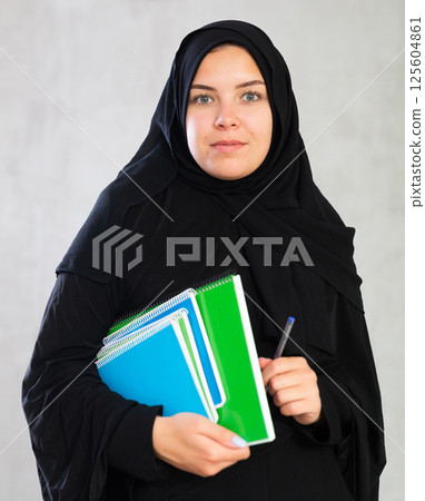 Young student woman dressed in traditional islamic clothes holding notebooks 125604861