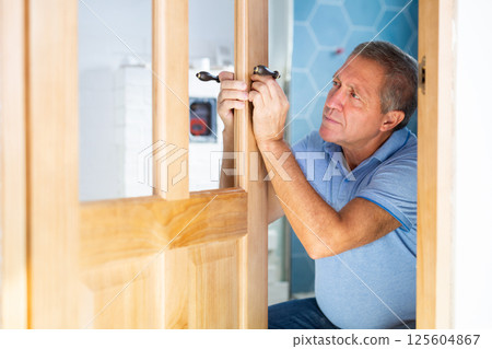 Man trying on door handles to install on new wooden door 125604867