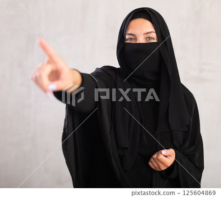 woman with her face covered by burka points her hand to side 125604869