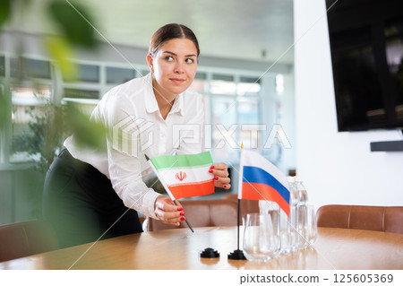 Young woman puts flags of Iran and Russia on table in office 125605369