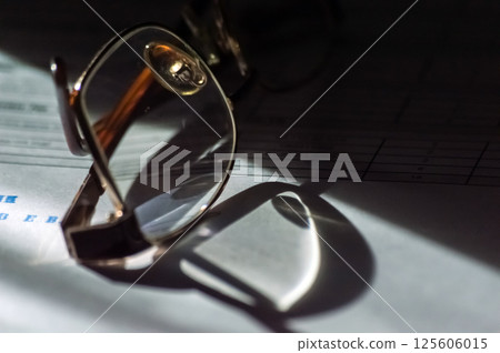 Glasses on the sheet of music with a shadow from the sun 125606015