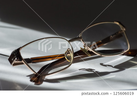 Eyeglasses with black frame on a white table in sunlight. Eyeglasses with black frame on a white table in sunlight. 125606019