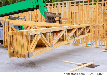 Telehandler crane raises wooden trusses at construction site during frame assembly building process. Telehandler crane raises wooden trusses at construction site during frame assembly building process. 125606028