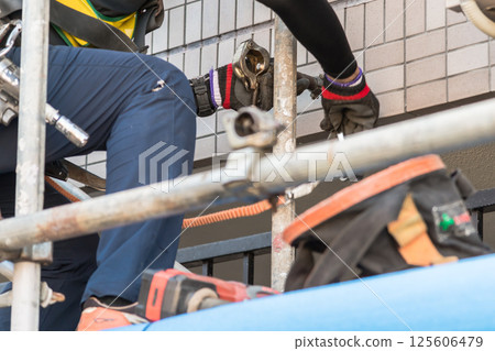 [Large-scale apartment building repair work: Workers connecting wall ties and building scaffolding] 125606479