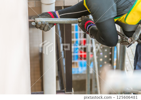[Large-scale apartment building repair work: Workers connecting wall ties and building scaffolding] 125606481