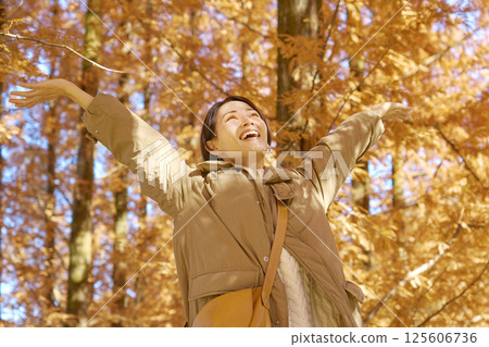 Middle-aged woman taking a deep breath among autumn leaves Middle-aged woman taking a deep breath among autumn leaves 125606736