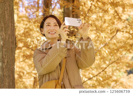 中年婦女用智慧型手機拍攝秋葉視頻 125606739