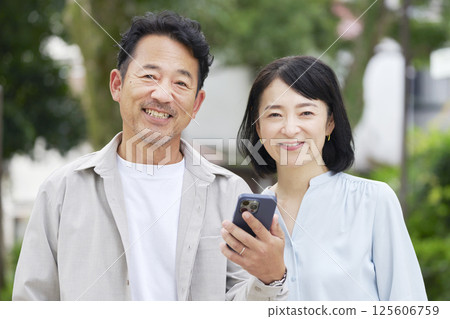 Middle-aged couple holding smartphones outdoors 125606759