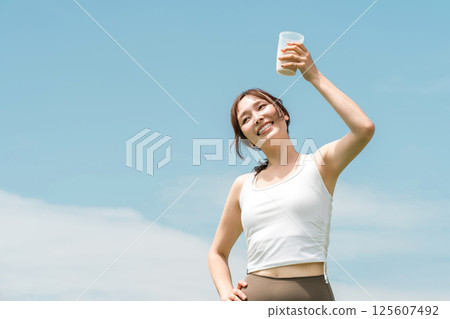 Woman drinking protein/EAA drink during exercise (blue sky) Woman drinking protein/EAA drink during exercise (blue sky) 125607492