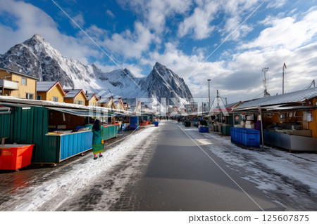 Winter landscape of a Scandinavian fishing port with a view of snowy mountains and a woman walking through a fish market 125607875