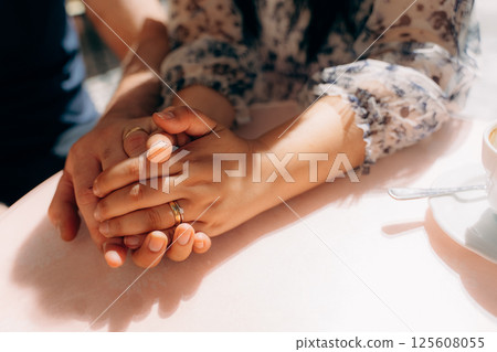 Couple Holding Hands with Wedding Rings at Cafe Table 125608055